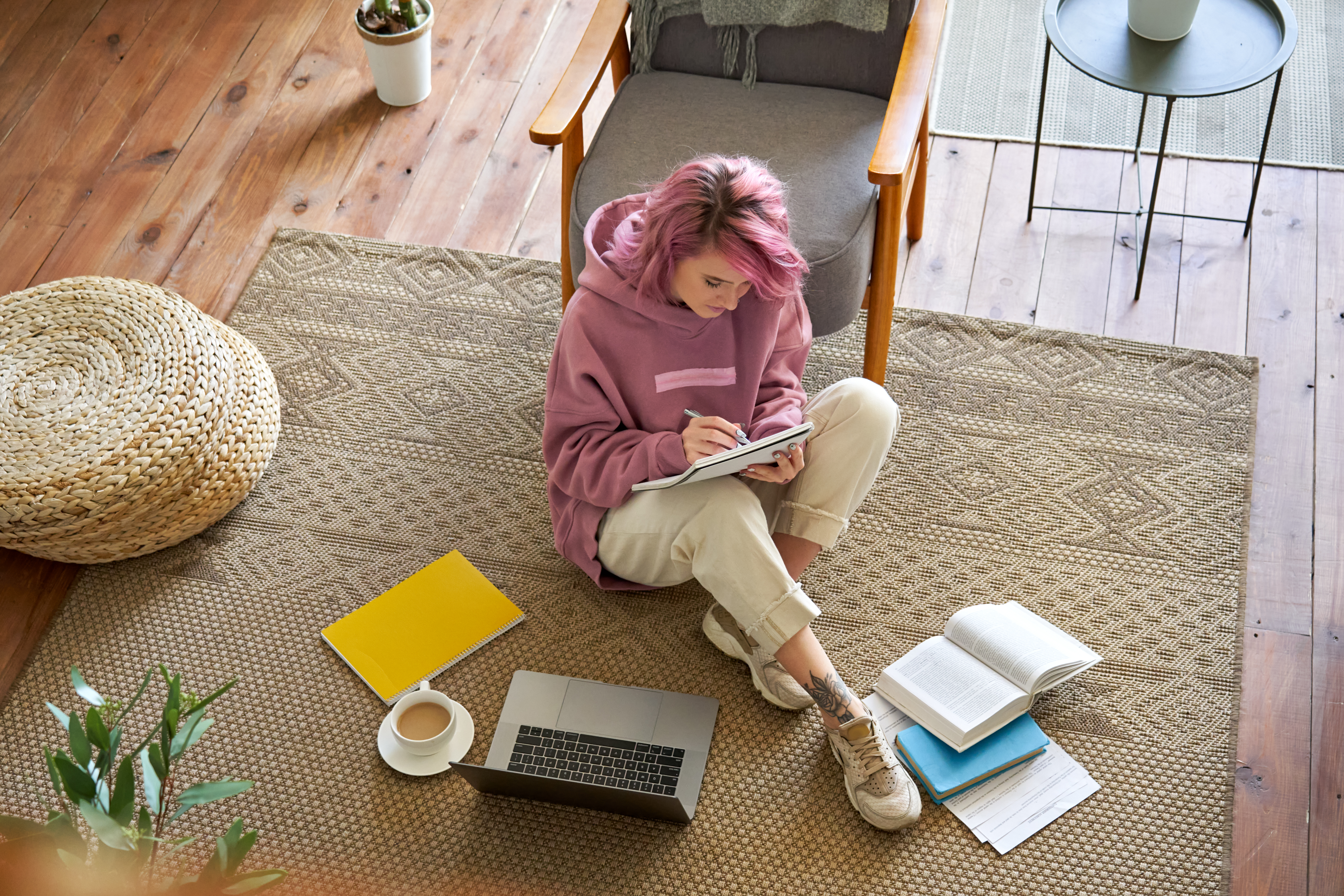 Teen girl studying online on laptop writing notes sit on floor, top view.