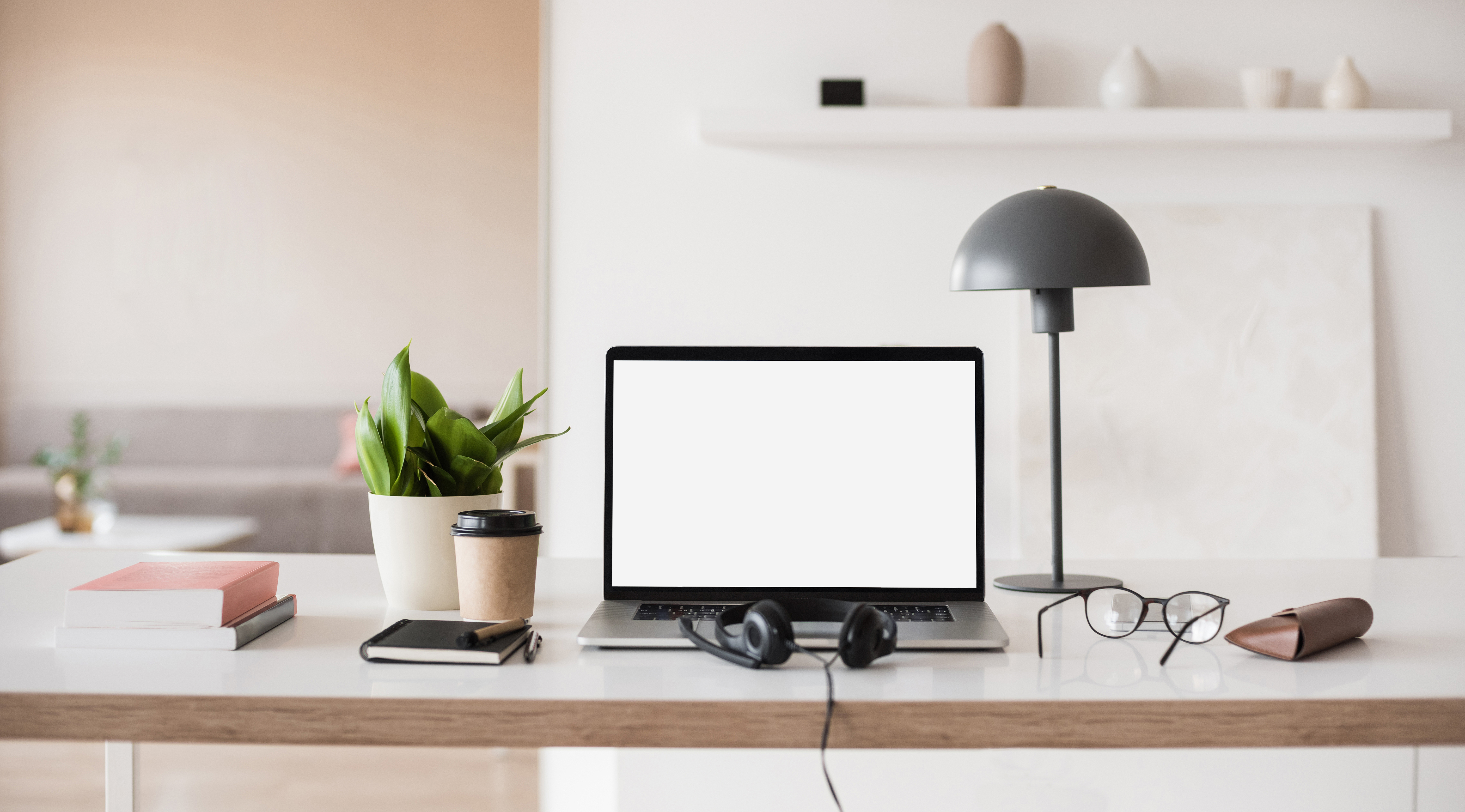 Image of a writing space in a light, modern room, with laptop, headphones, coffee, books and a desk lamp arranged neatly on a table