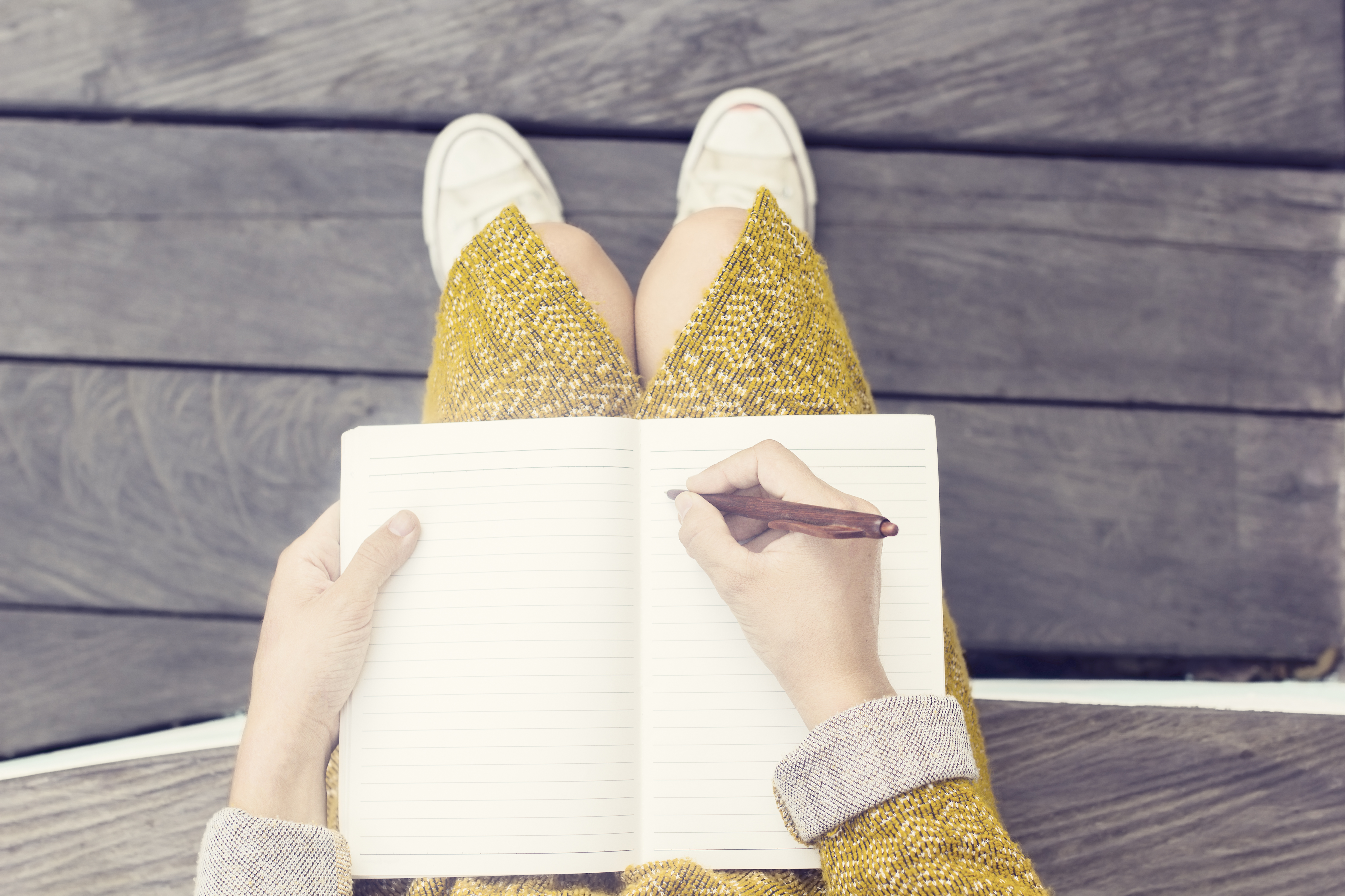 Close-up image of a notebook open in a woman's lap, with her pen poised to start writing on a blank page