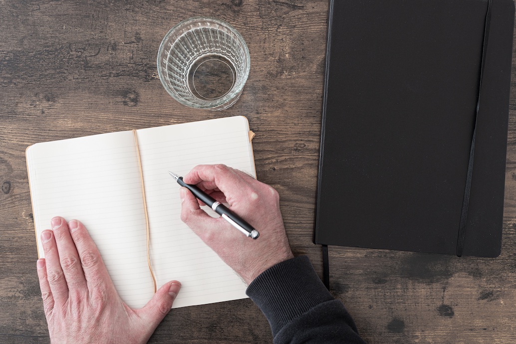 above view of person at wooden desk taking notes in diary or journal