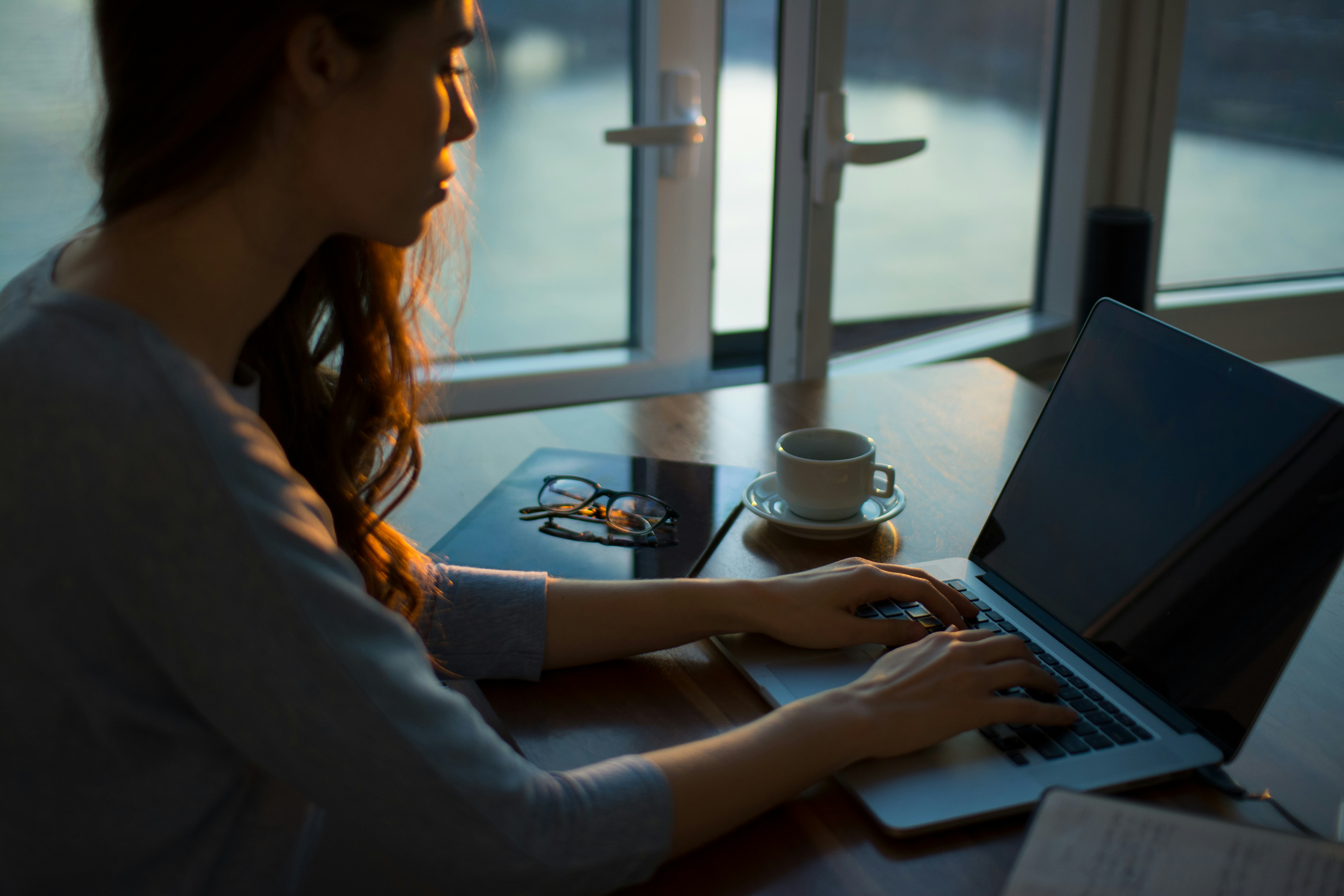Woman typing on a laptop with spectacles and a cup of tea on table