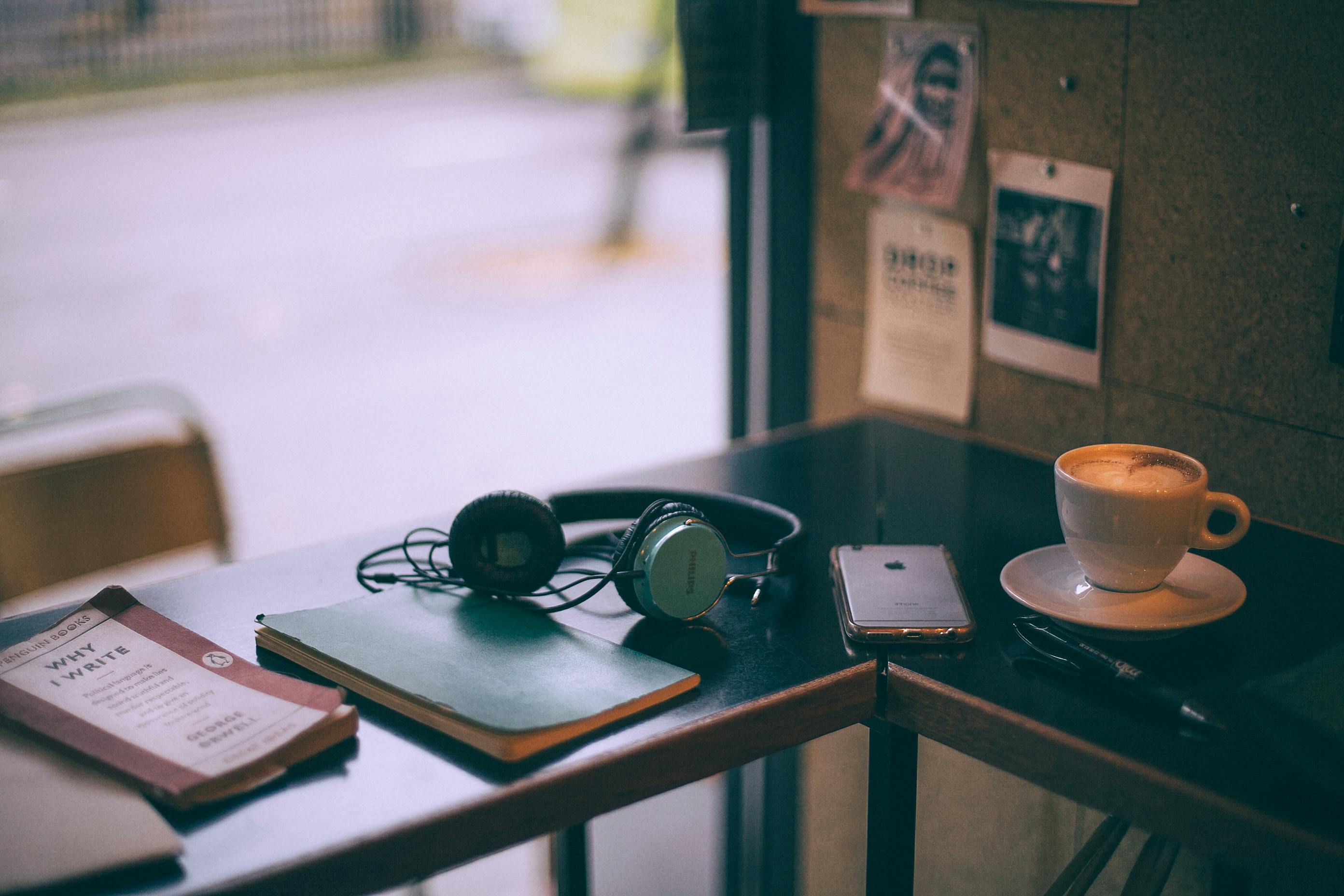 Notebook, pen, headphones, phone, book and coffee on a table